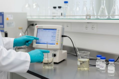 Científico con guantes utilizando un pH-metro digital para analizar muestras líquidas en un laboratorio