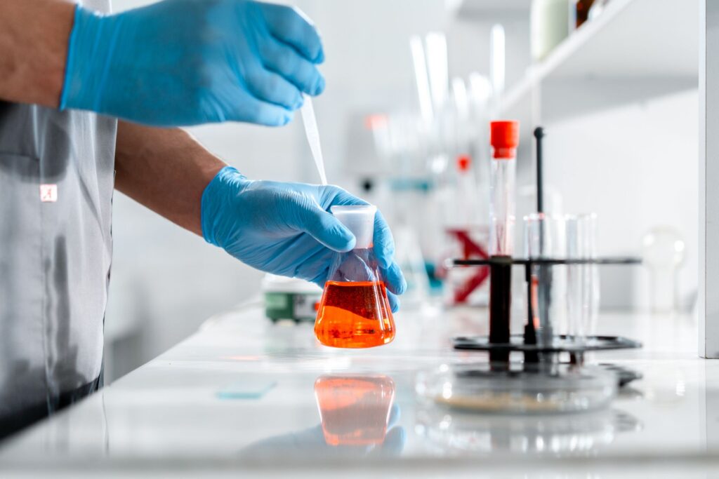 Chemist dosing a flask of orange liquid with a pipette in a laboratory