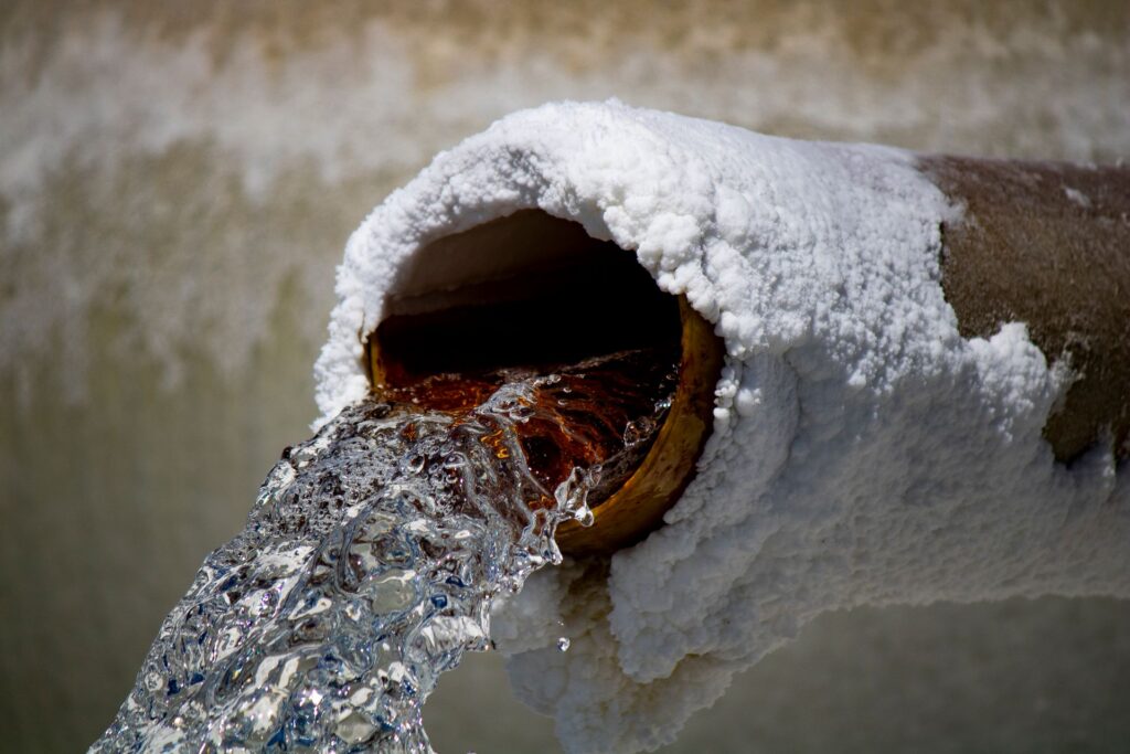 Water flowing from a pipe crusted with white mineral scale deposits