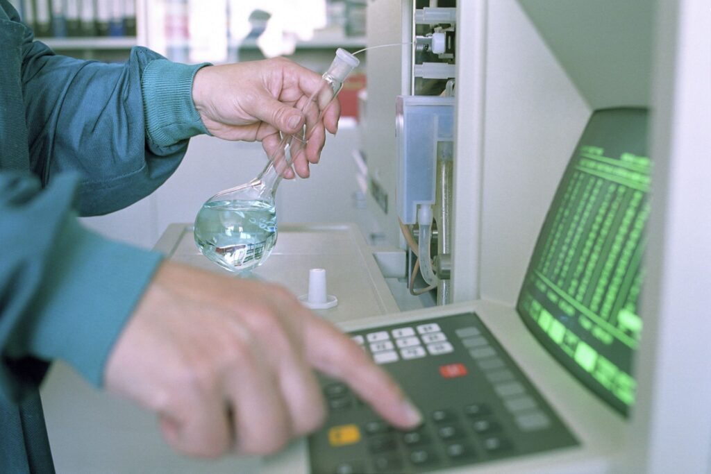 Lab technician holding a flask at an analytical instrument, testing a water sample